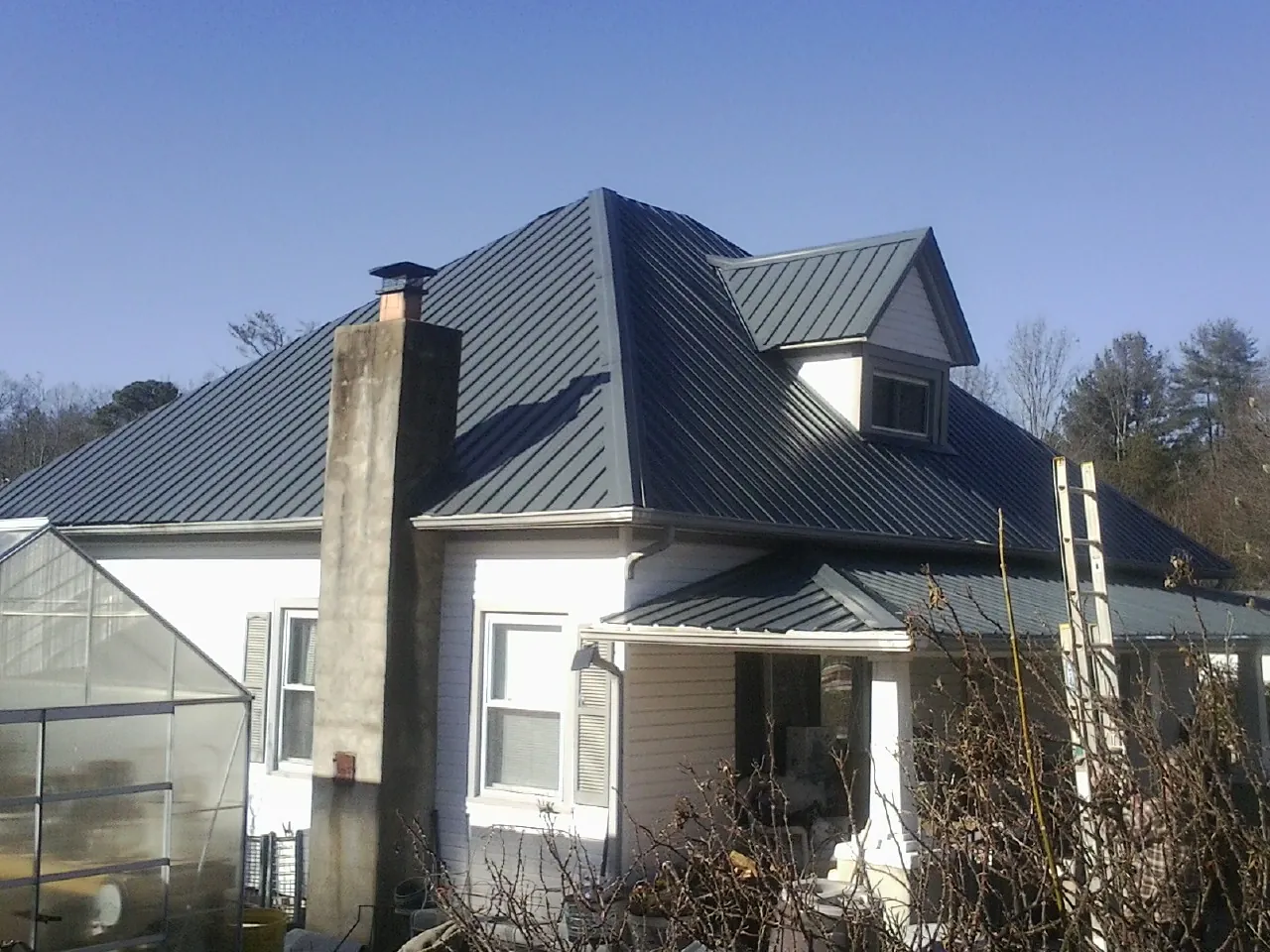 Dark blue standing seam metal roof on a white farmhouse with dormer — Slate & Tile Roof Repair by Roofing Brothers in Montpelier