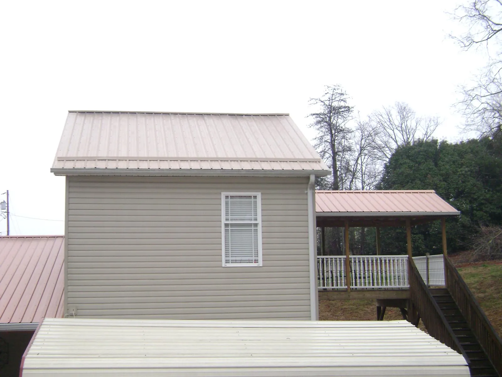 Tan metal roofs on a two story addition and attached porch, from a Roof Replacement job in Montpelier